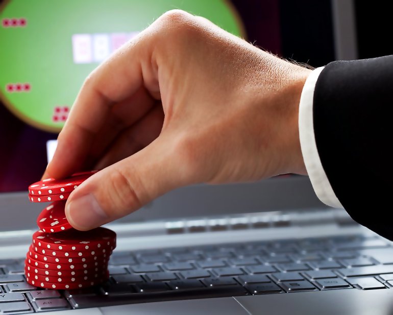 Hand stack of red chips and online poker on laptop